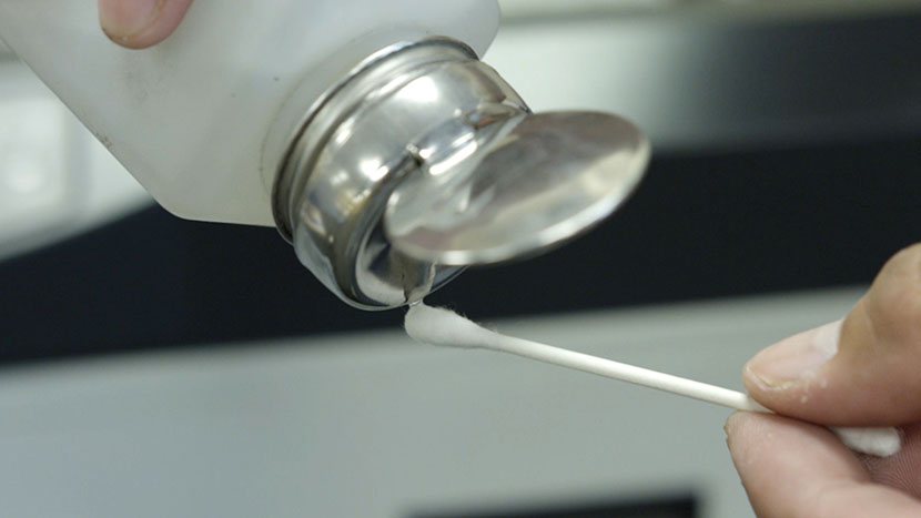 Pouring rubbing alcohol onto a cotton swab.