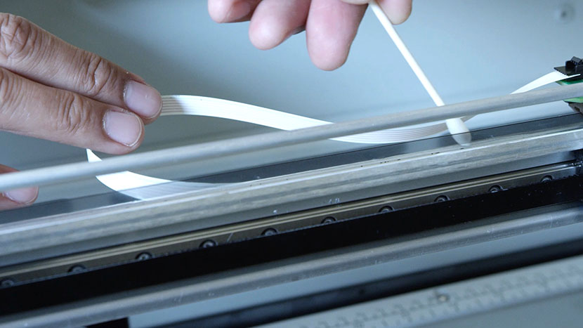 Using a cotton swab to clean the back of the linear encoder strip.