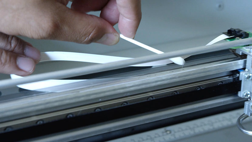 Using a cotton swab to clean the top of the linear encoder strip.