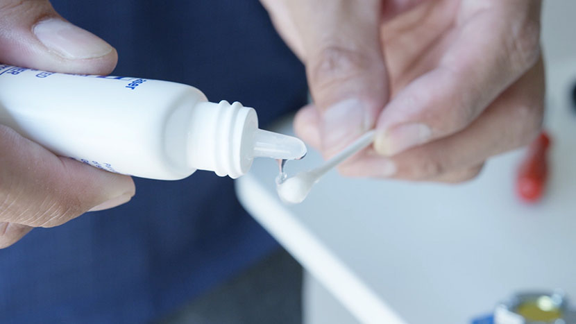 Applying lens cleaning fluid to a cotton swab.