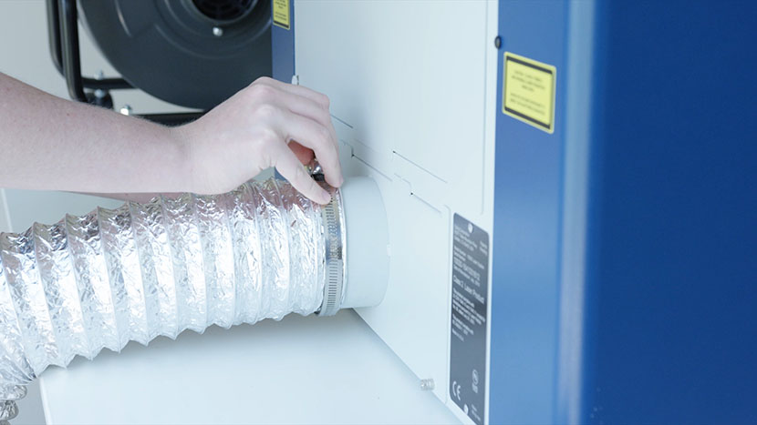 An air ducting tube being attached to the exhaust port on the Epilog Laser Zing.