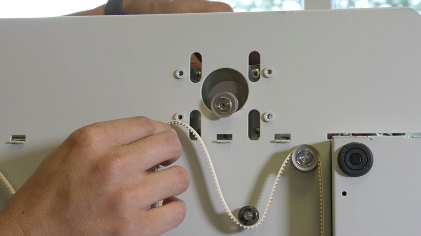 The table motor sticking through the bottom of the machine, with the belt about to be looped around its pulley.